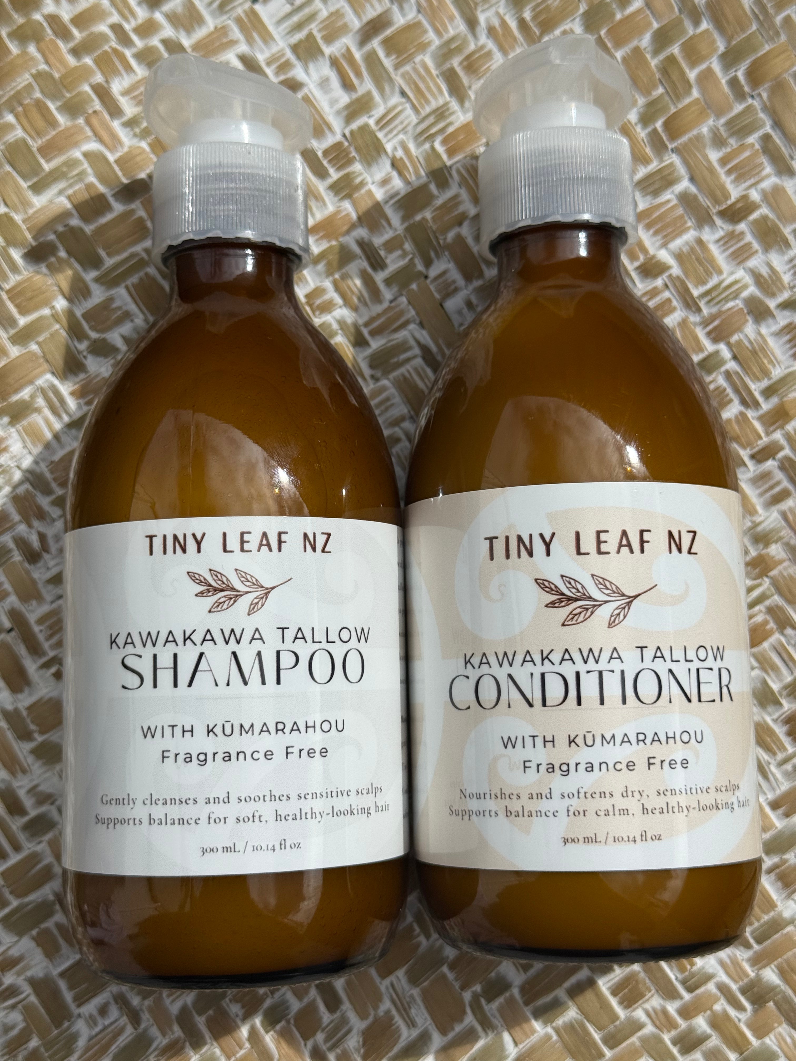 Two amber plastic bottles of Tiny Leaf Nz hair care products, labeled Kawakawa Tallow Shampoo and Kawakawa Tallow Conditioner, placed side by side on a woven tan mat.