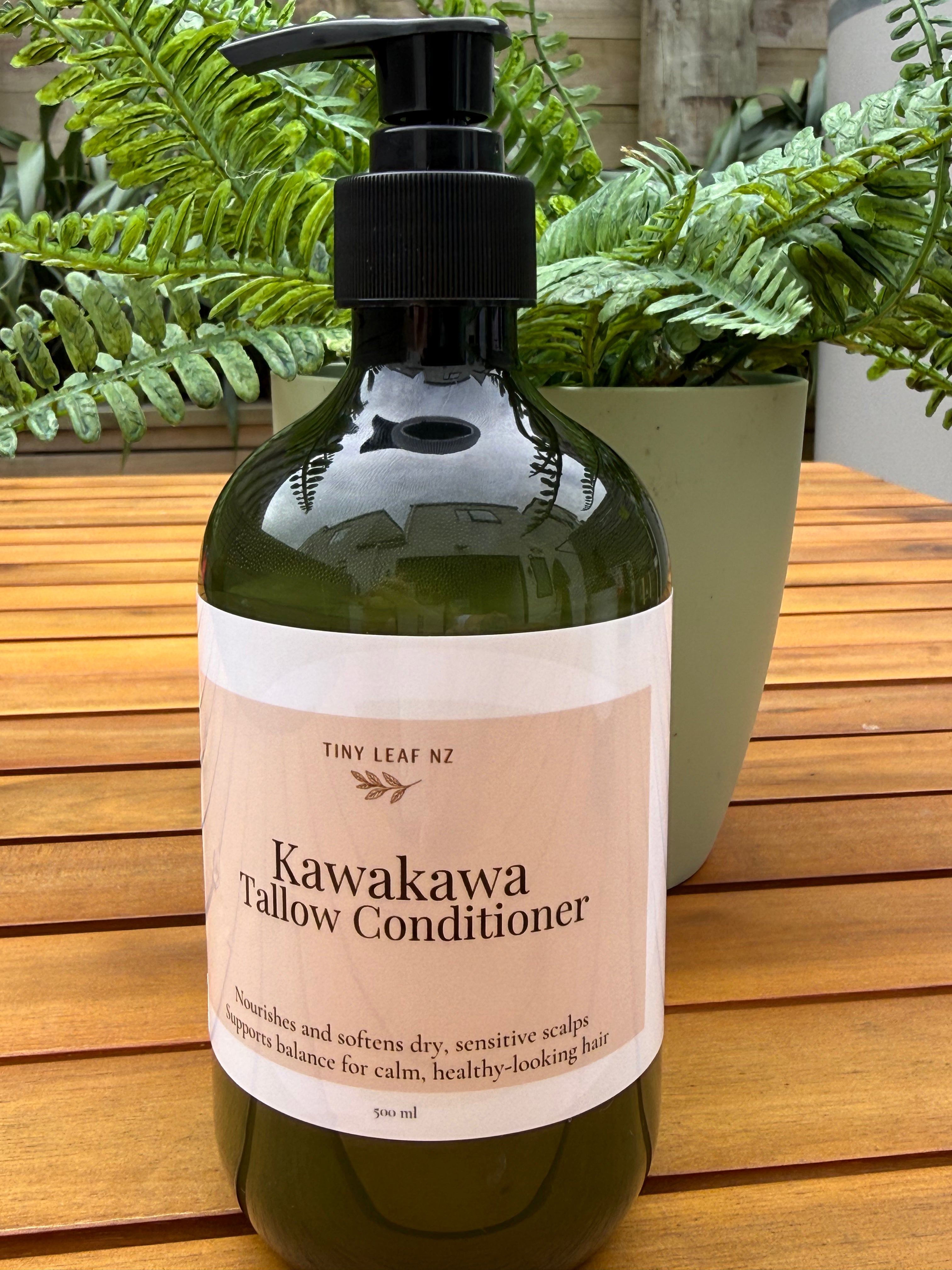 Bottle of Kawakawa Tallow Conditioner with a pump on a wooden surface with plants in the background