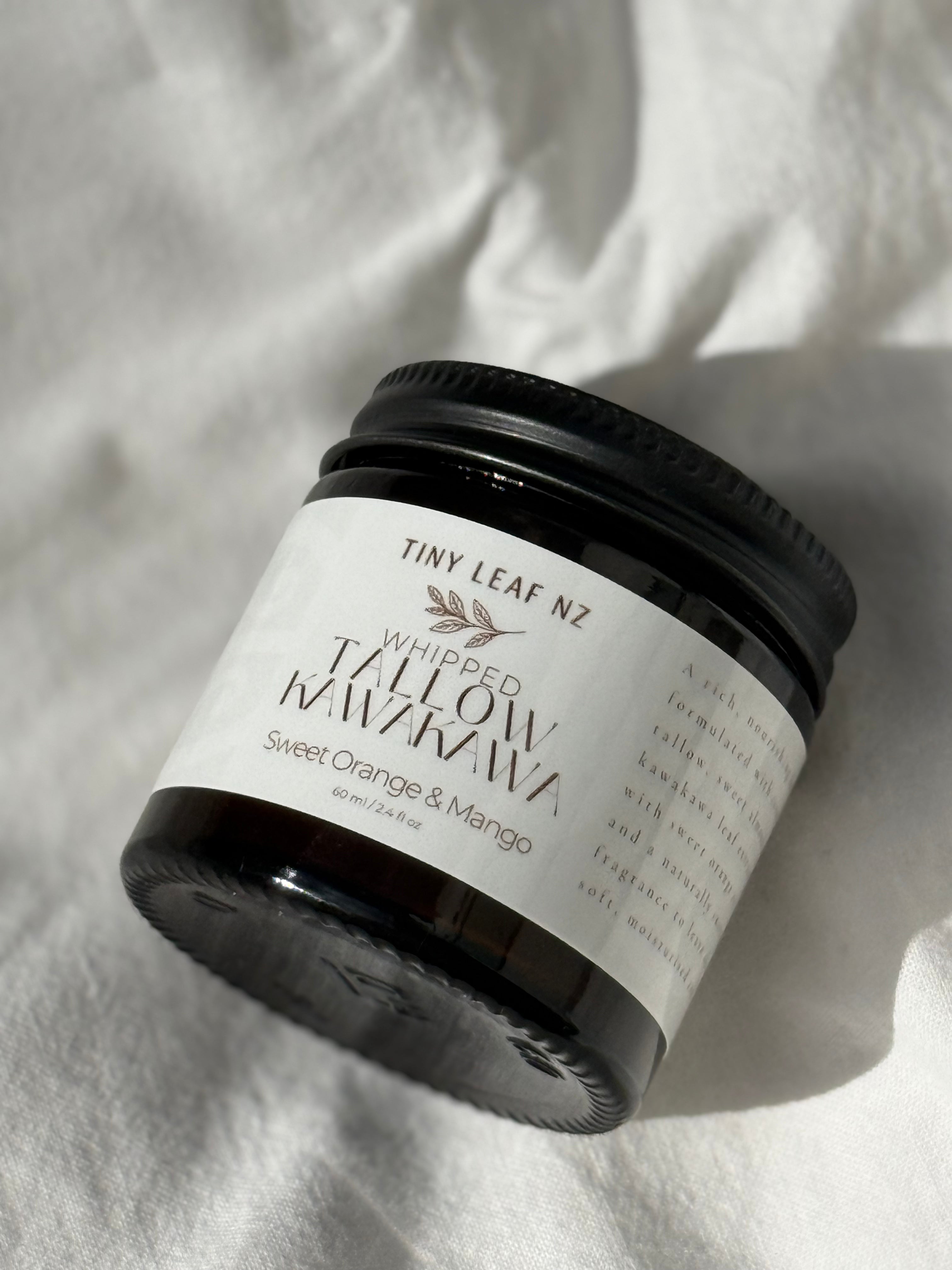 A jar of Tiny Leaf NZ Whipped Tallow Manuka Sweet Orange & Mango scented soap, shown on a textured white fabric background with a soft shadow.