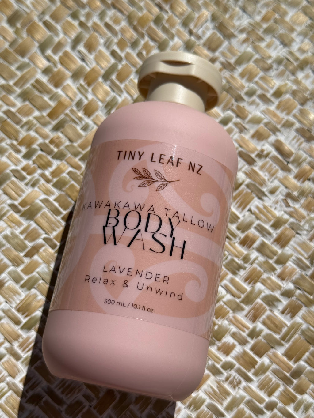 A bottle of Tiny Leaf Nz Kawakawa Tallow Body Wash in Lavender, shown on a woven straw mat background.