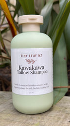 A bottle of Tiny Leaf NZ Kawakawa Tallow Shampoo, featuring a pale sage green bottle and a white label, set against a background of green leaves.