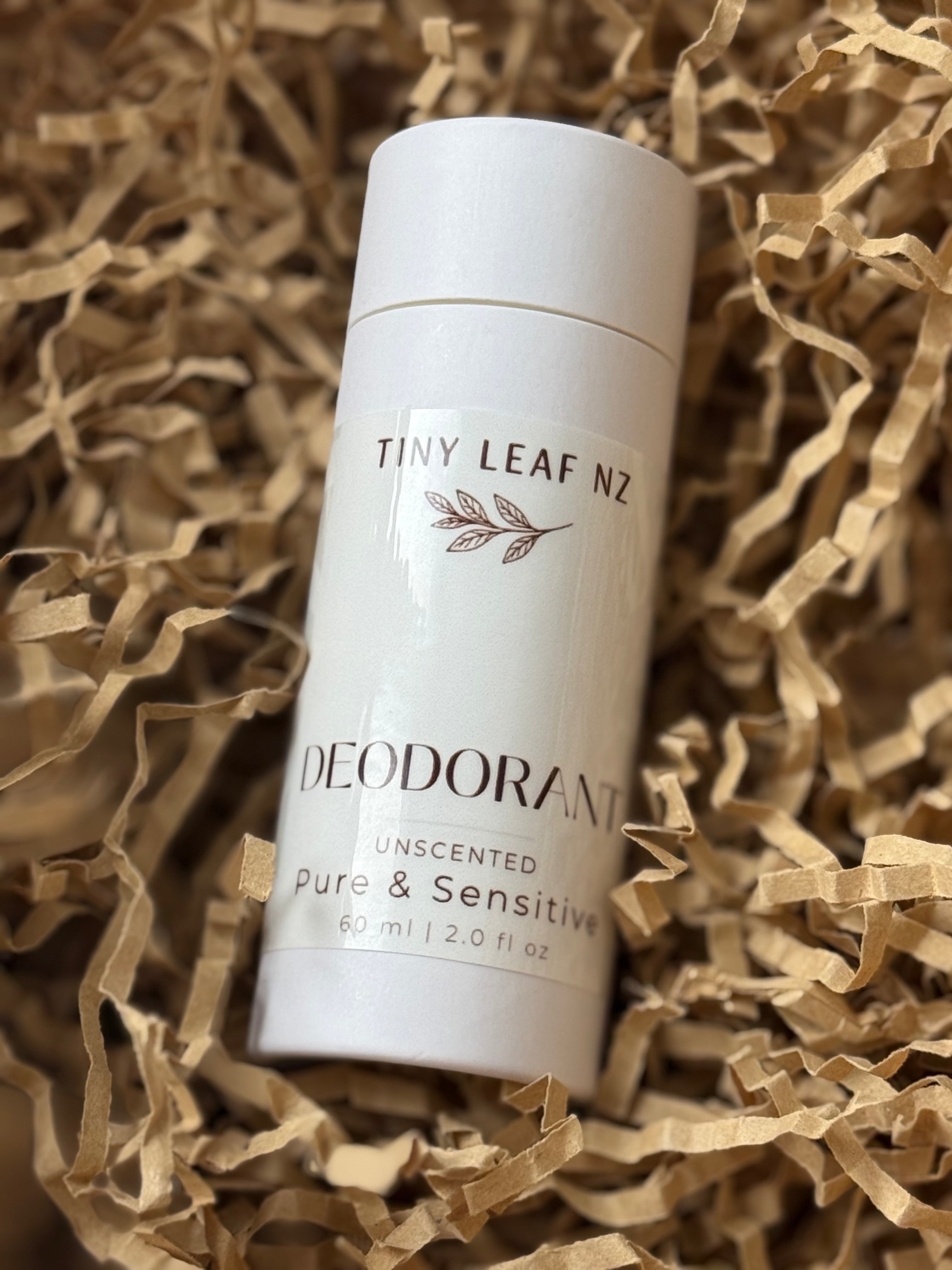 A white cylindrical deodorant stick labeled 'TINY LEAF NZ' and 'DEODORANT' with 'Pure & Sensitive' and 'Unscented' printed on it, placed on brown shredded paper filler.