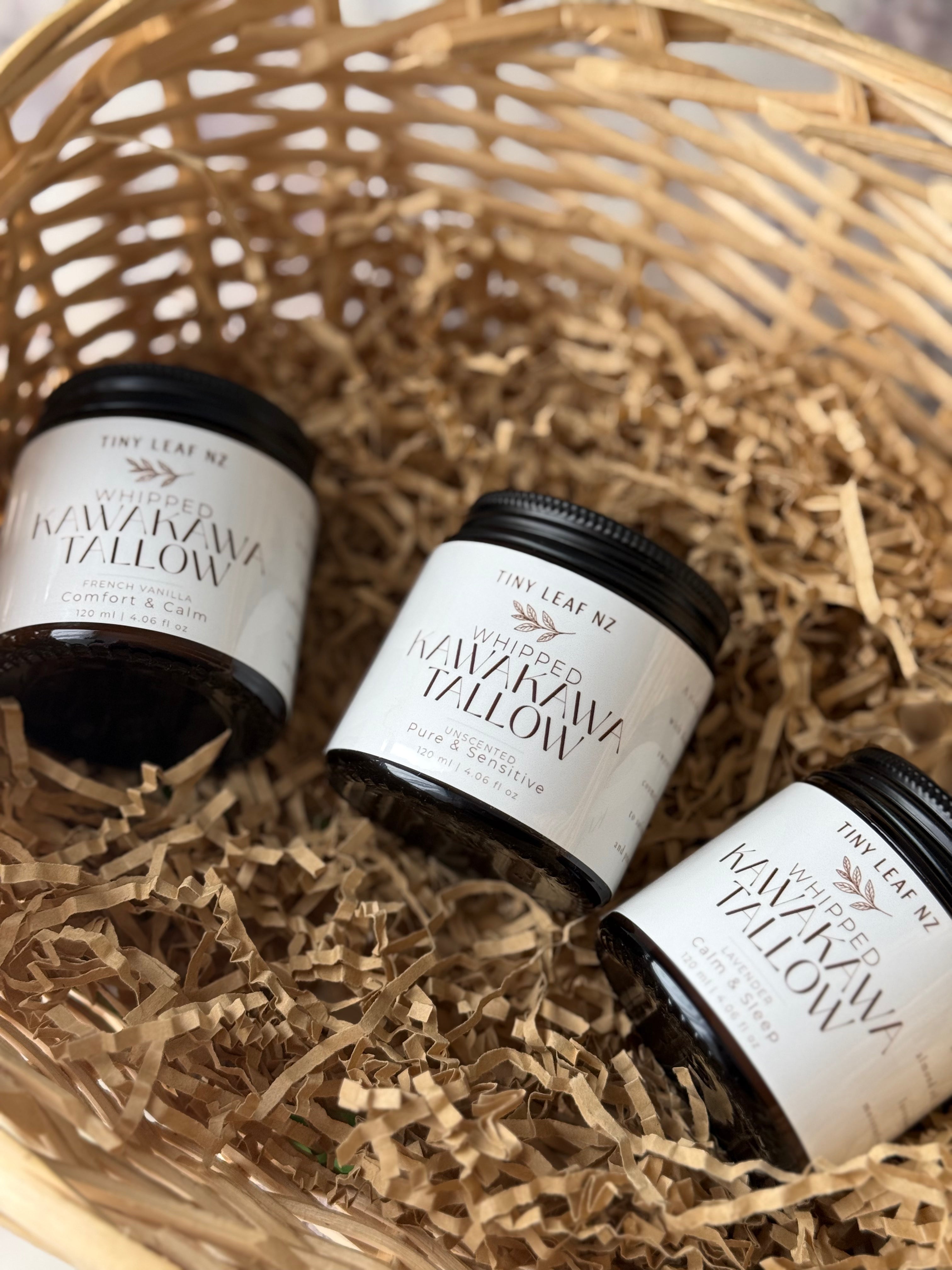 Three small jars of Tiny Leaf NZ Whipped Kawakawa tallow balm arranged in a woven basket with shredded paper filler.