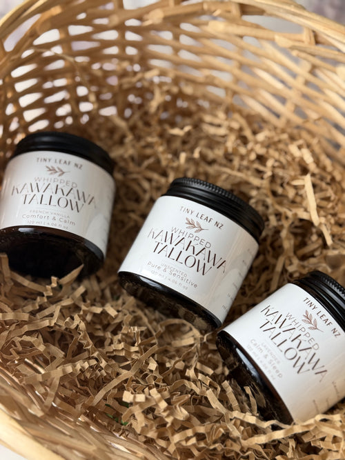 Three small jars of Tiny Leaf NZ Whipped Kawakawa tallow balm arranged in a woven basket with shredded paper filler.