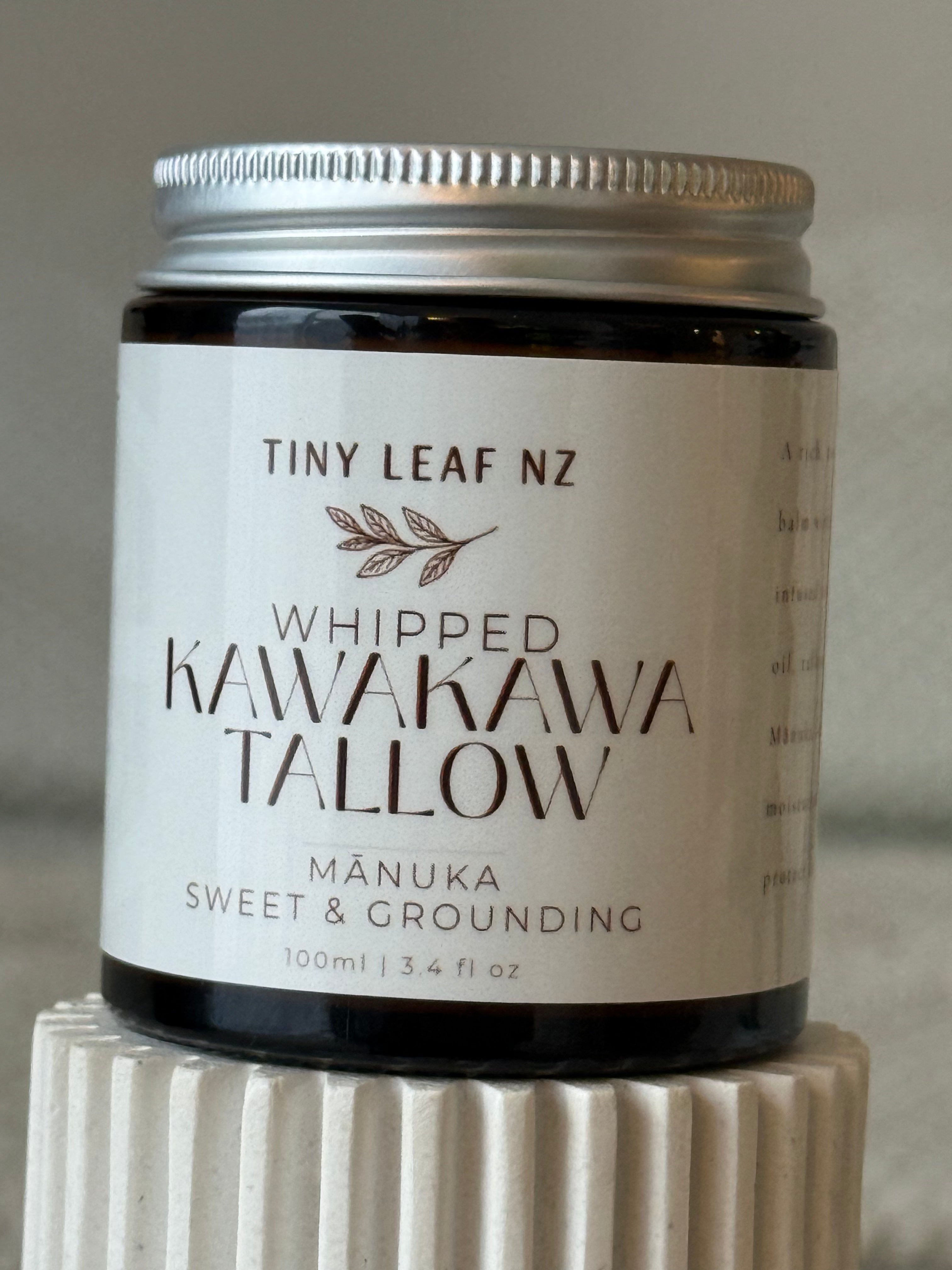A jar of Tiny Leaf NZ Whipped Kawakawa Tallow (Mâuka Sweet & Grounding) with a white label and silver lid, displayed on a textured white pedestal.
