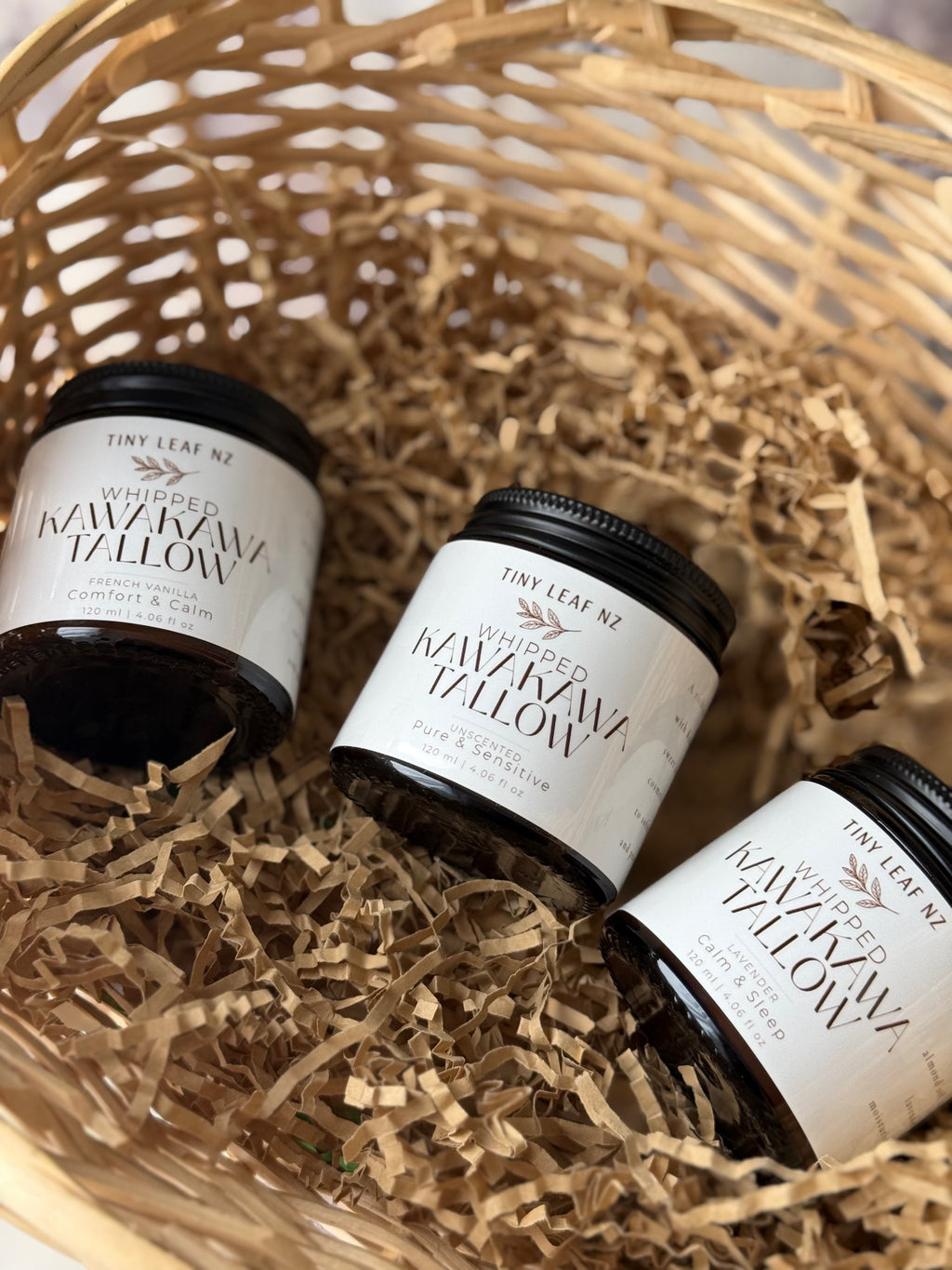 Three small jars of whipped kawaka yellow from Tiny Leaf NZ, arranged in a woven basket filled with brown paper shred.