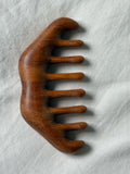 A hand-carved wooden hair comb with a rich medium brown finish and visible wood grain, resting on a textured white fabric background.