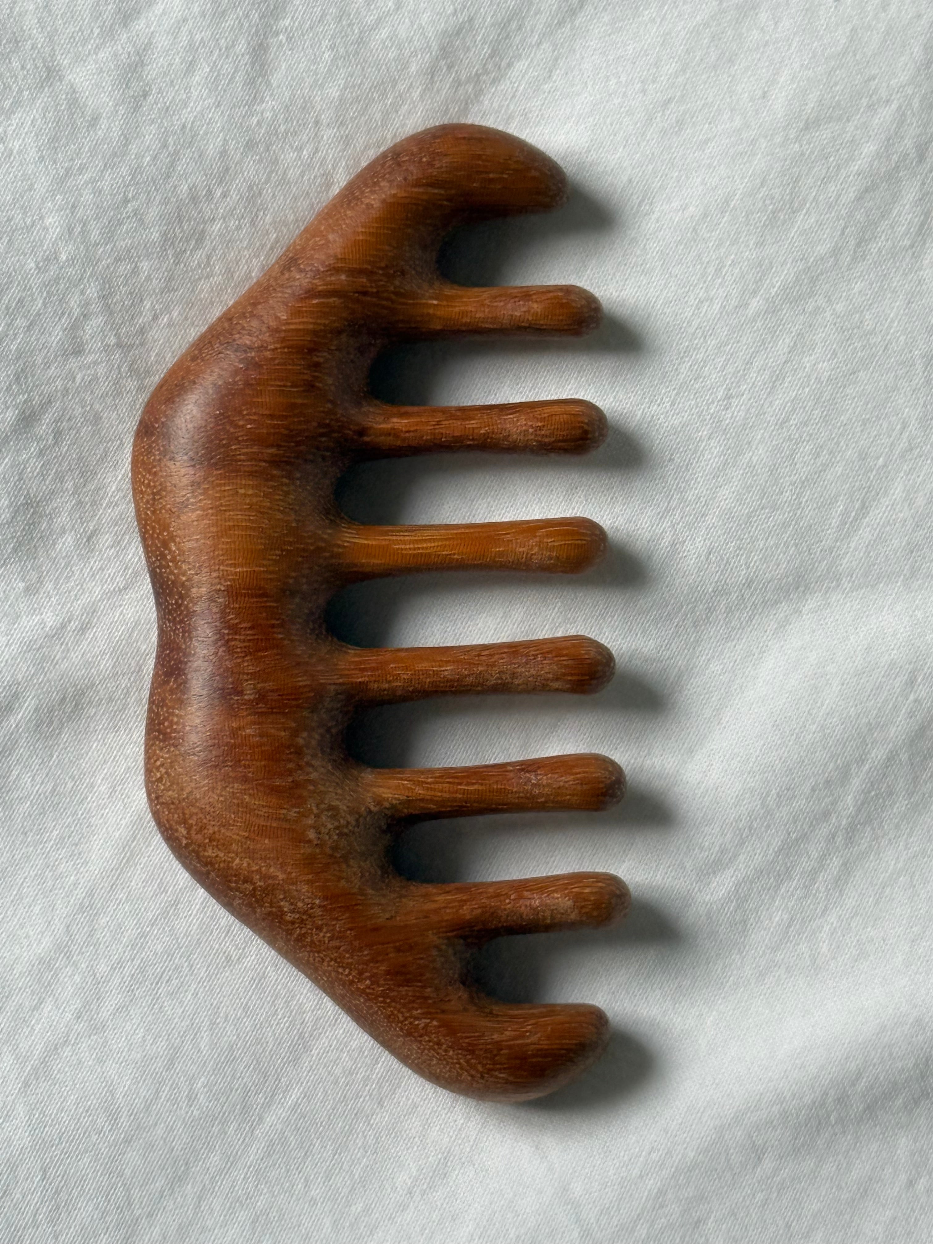 A hand-carved wooden hair comb with a rich medium brown finish and visible wood grain, resting on a textured white fabric background.