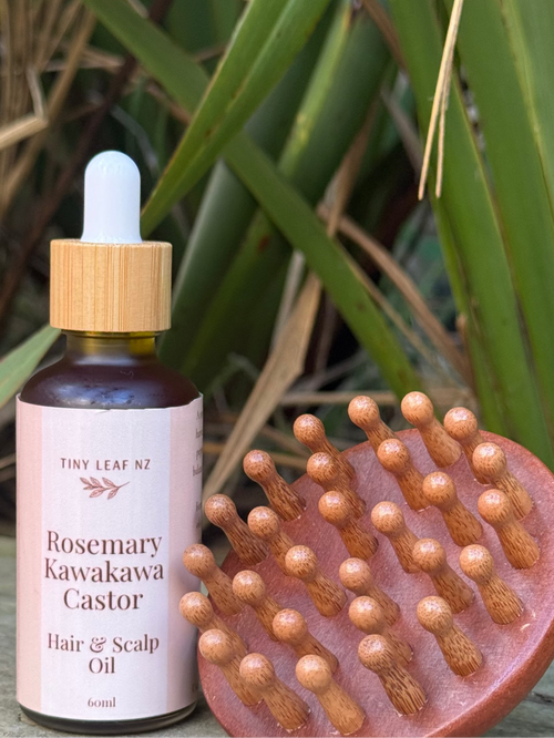 Hair oil bottle and scalp massage brush on a wooden surface with green plants in the background