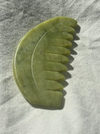 A jade hair comb made of polished green jade, resting on a textured white fabric under direct sunlight.