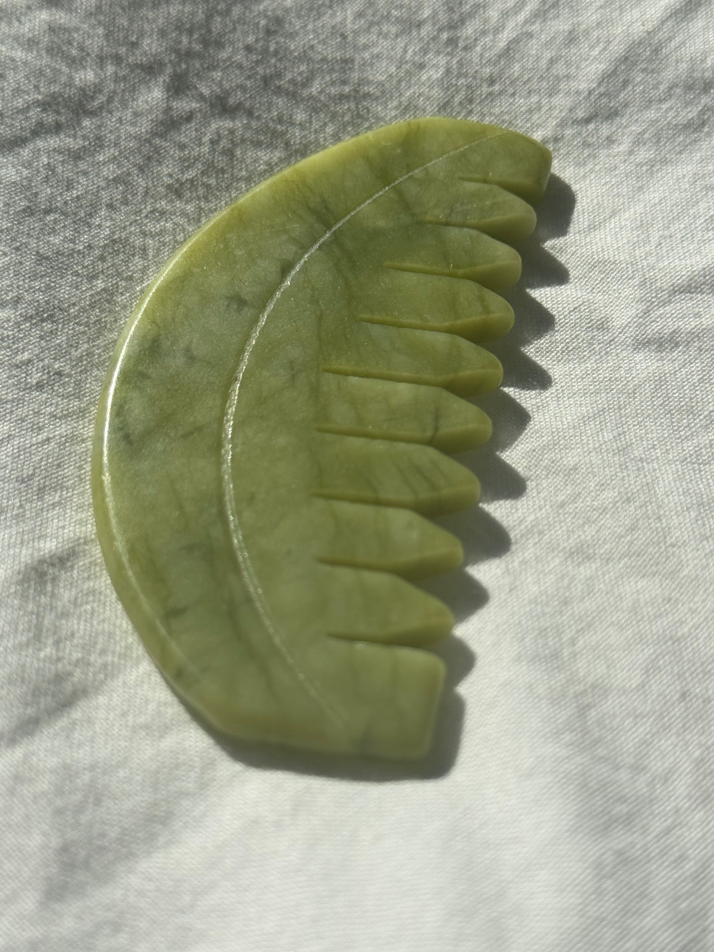 A jade hair comb made of polished green jade, resting on a textured white fabric under direct sunlight.