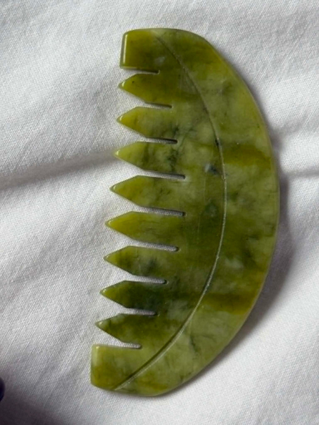 Green jade tool with serrated edges on a white fabric background