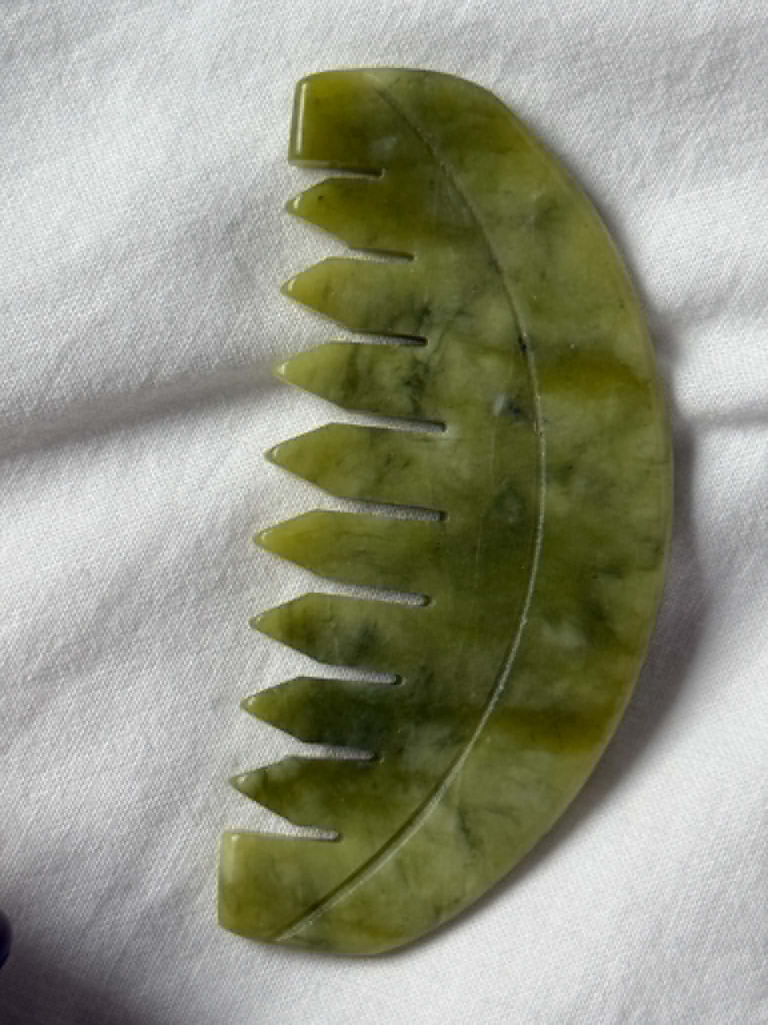 Green jade tool with serrated edges on a white fabric background