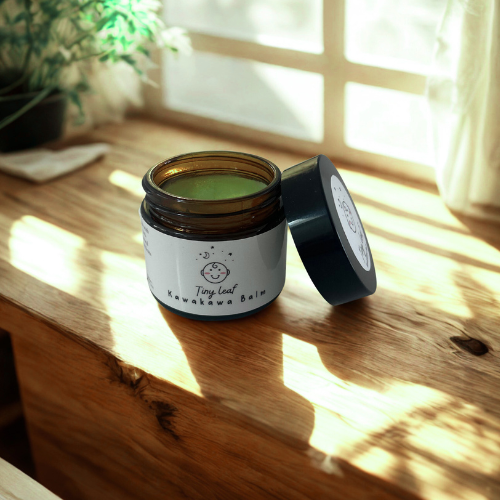 jar of kawakawa balm sitting on a wooden surface with sunlight radiating in background