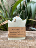 Bar of soap with a label on a wooden surface with greenery in the background