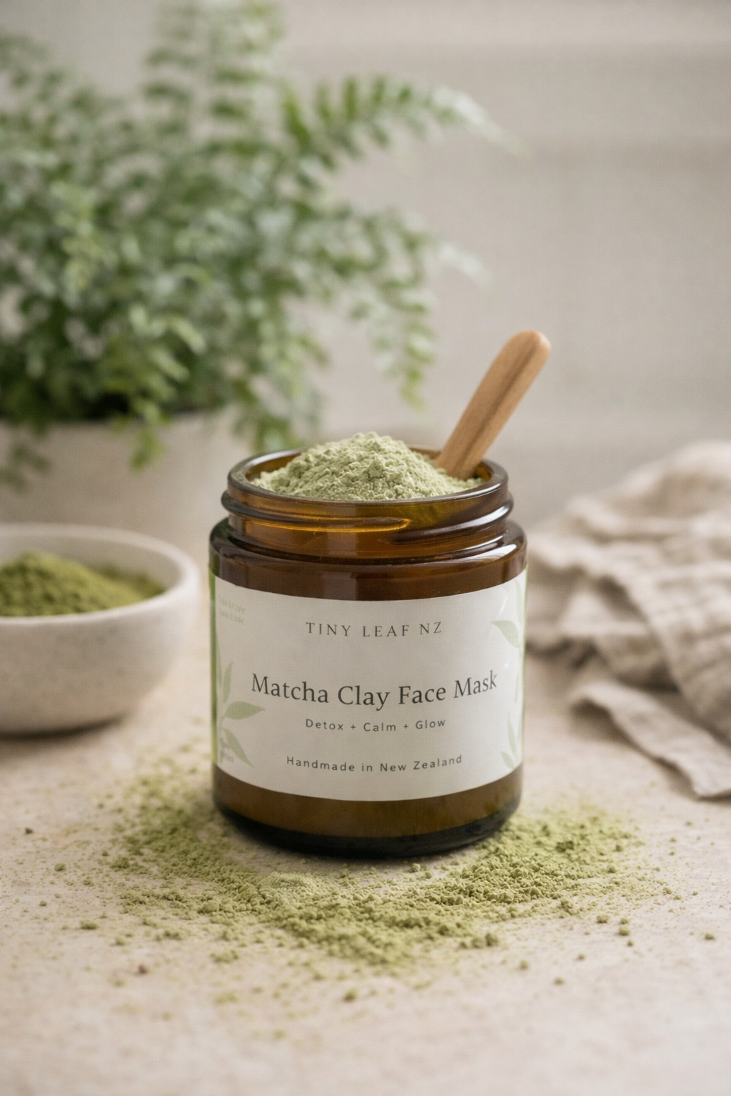 Jar of Tiny Leaf NZ Matcha Clay Face Mask with a wooden spoon on a neutral background