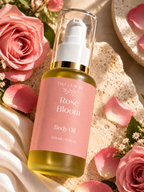 A bottle of Tiny Leaf N2 Rose Bloom Body Oil, filled with golden-yellow oil and featuring a pink label, styled with pink roses, petals, and a textured stone surface.