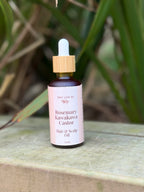 Bottle of Rosemary Kawakawa Castor Hair & Scalp Oil on a wooden surface with green leaves in the background