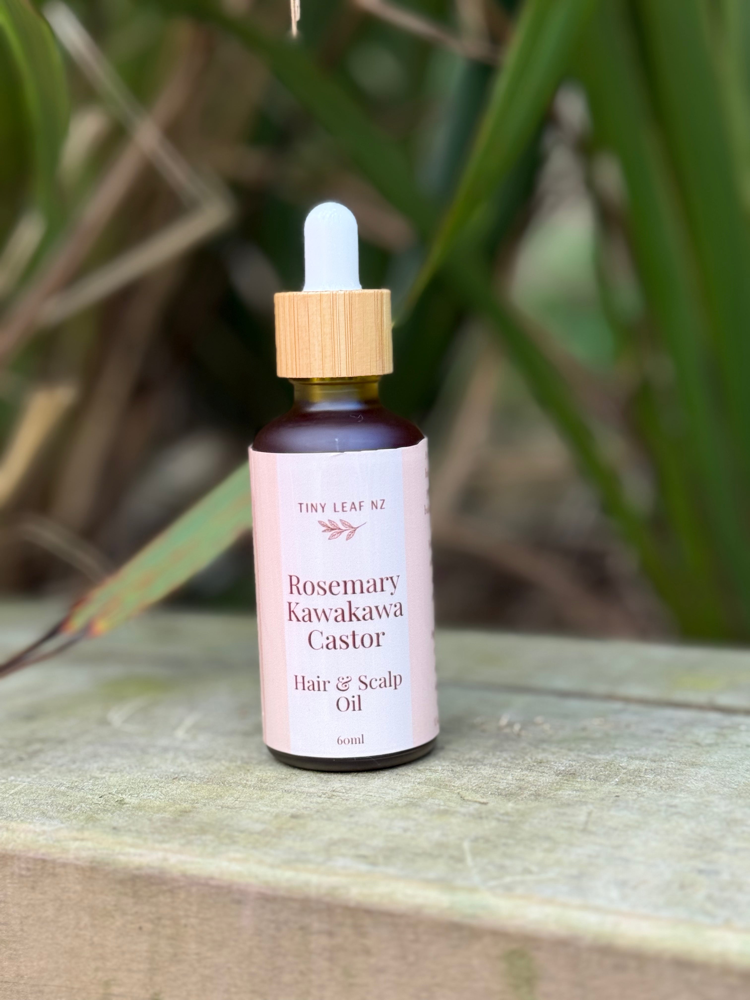 Bottle of Rosemary Kawakawa Castor Hair & Scalp Oil on a wooden surface with green leaves in the background
