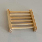A miniature wooden ladder soap holder made of light natural wood, photographed on a neutral light gray background.