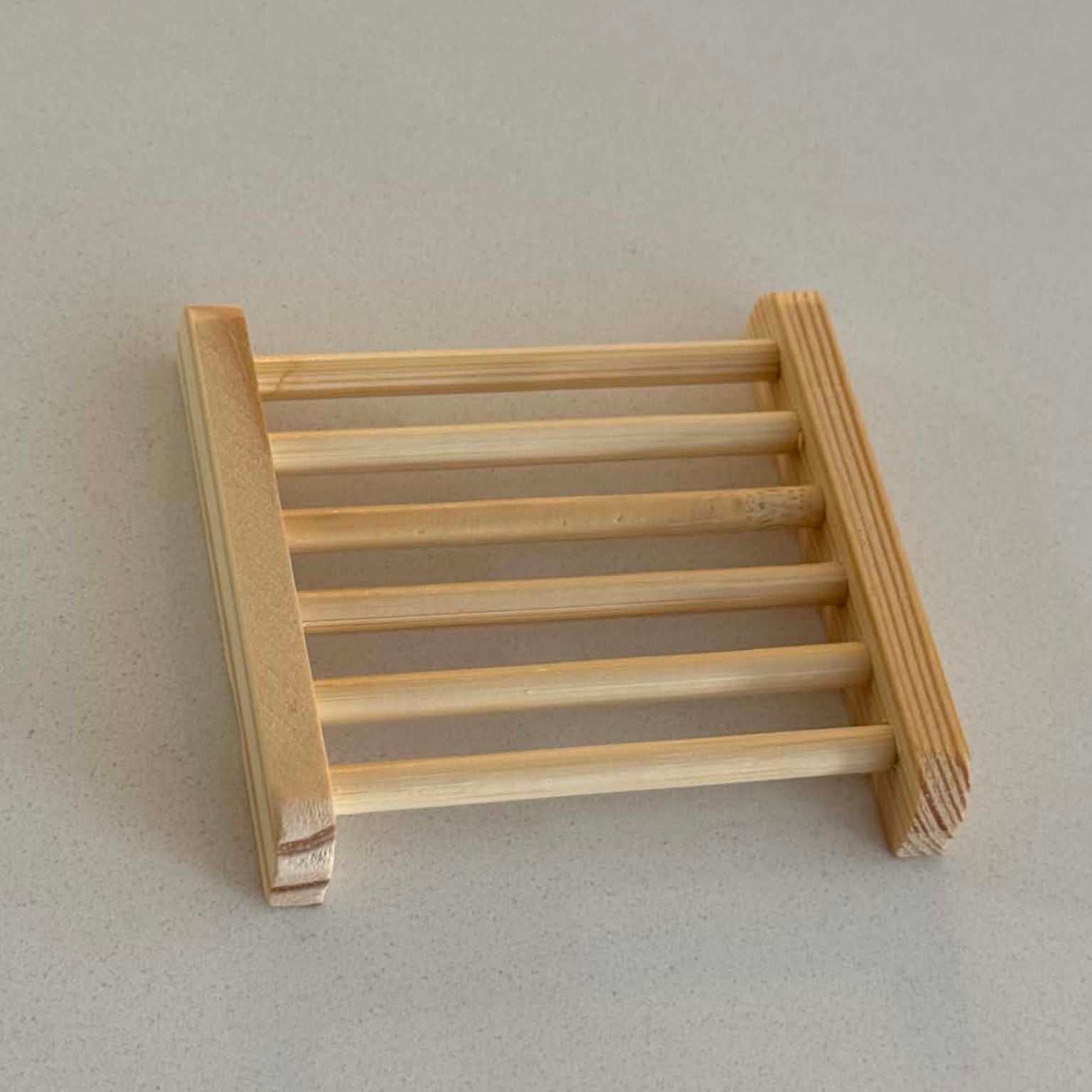 A small wooden ladder-style soap rack of light natural wood, photographed on a plain light gray surface.