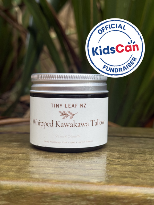 A jar of Tiny Leaf NZ Whipped Kawakawa Tallow (Peach Vanilla) sits on a wooden surface with a green leafy background. An official KidsCan Fundraiser badge is overlaid in the top right corner.