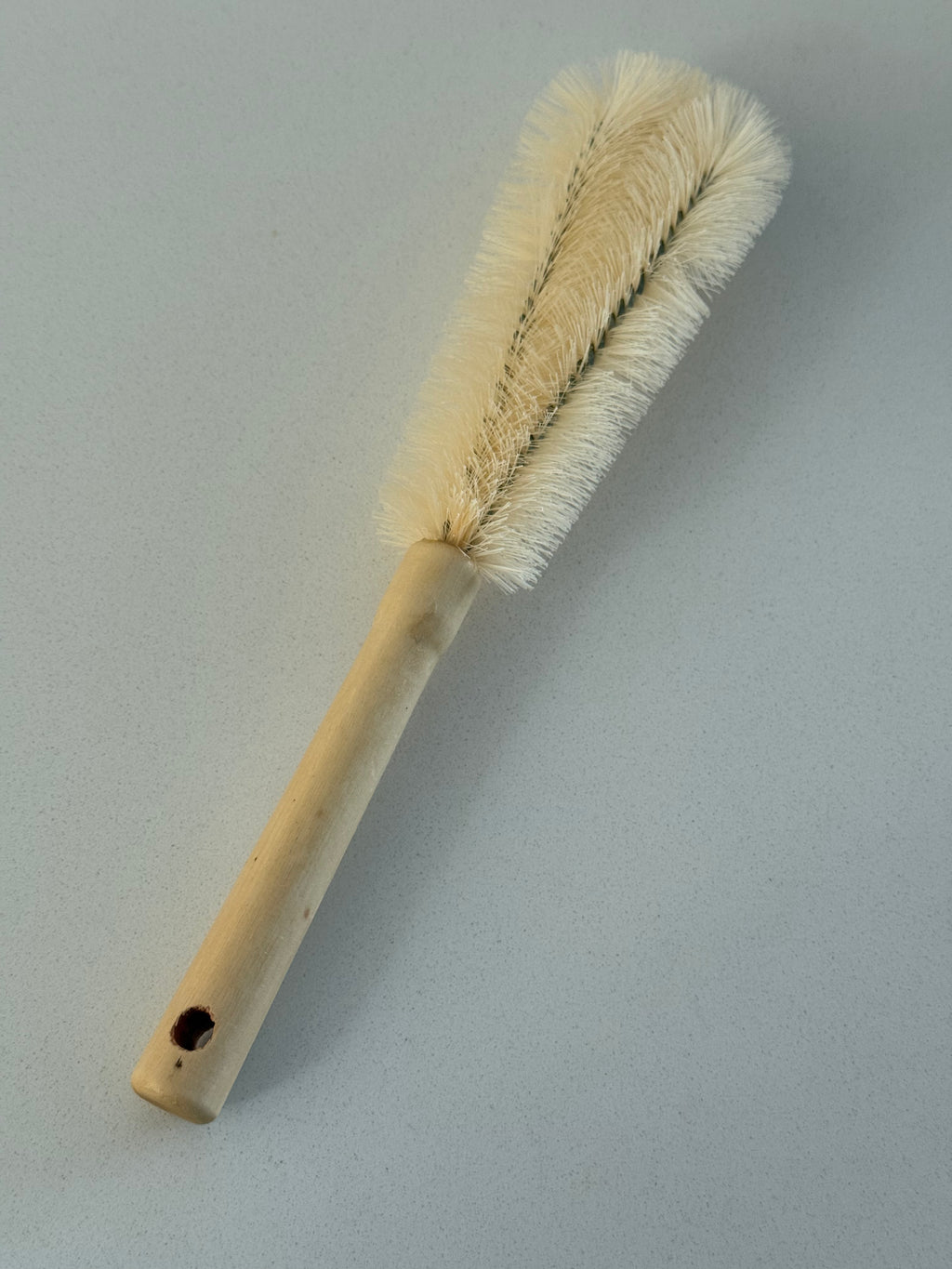 A wooden-handled cleaning brush with cream-colored bristles, shown diagonally on a plain light gray background.