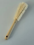 A wooden-handled cleaning brush with cream-colored bristles, shown diagonally on a plain light gray background.