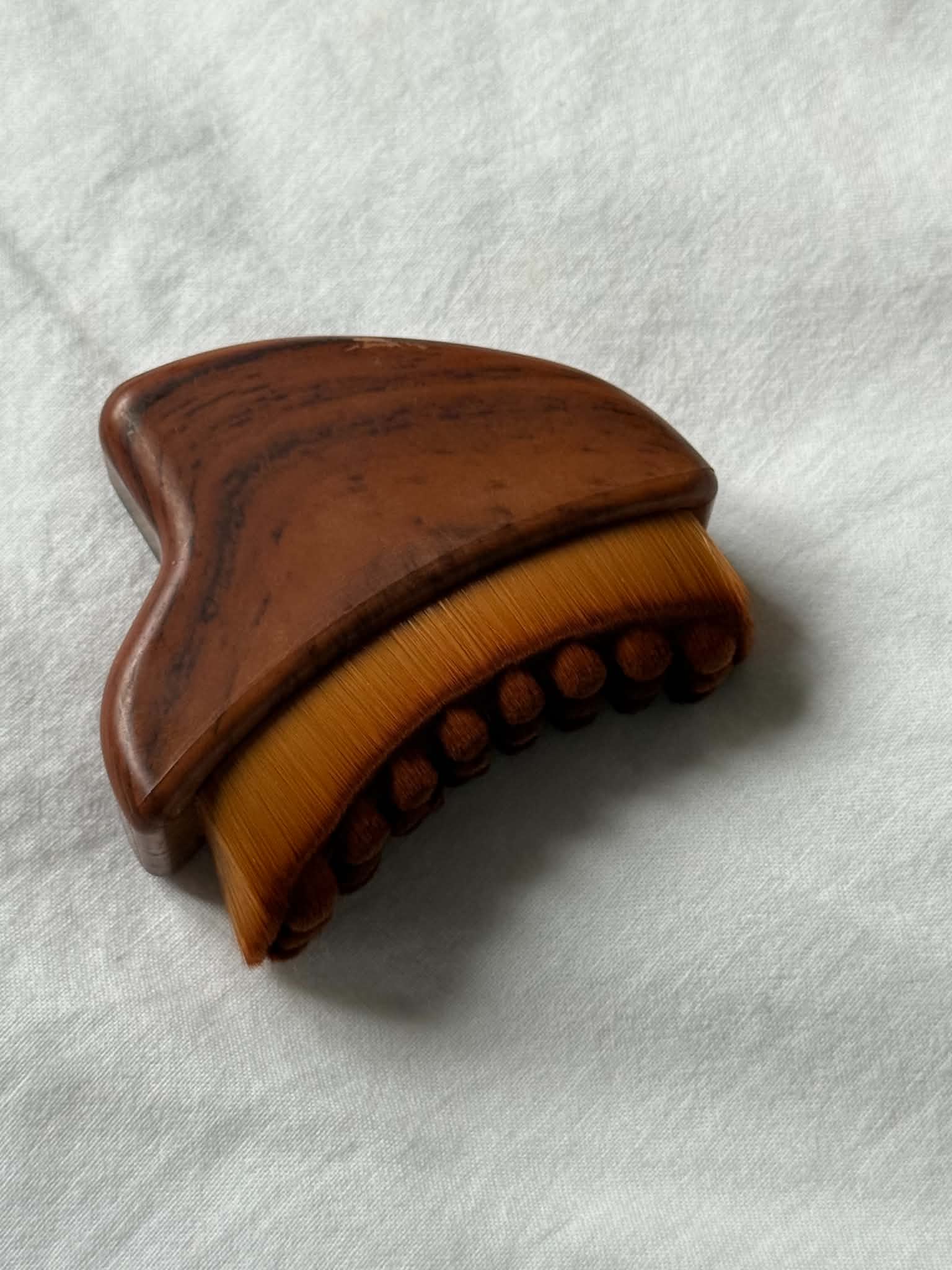 Wooden brush with brown handle and orange bristle head on a white background