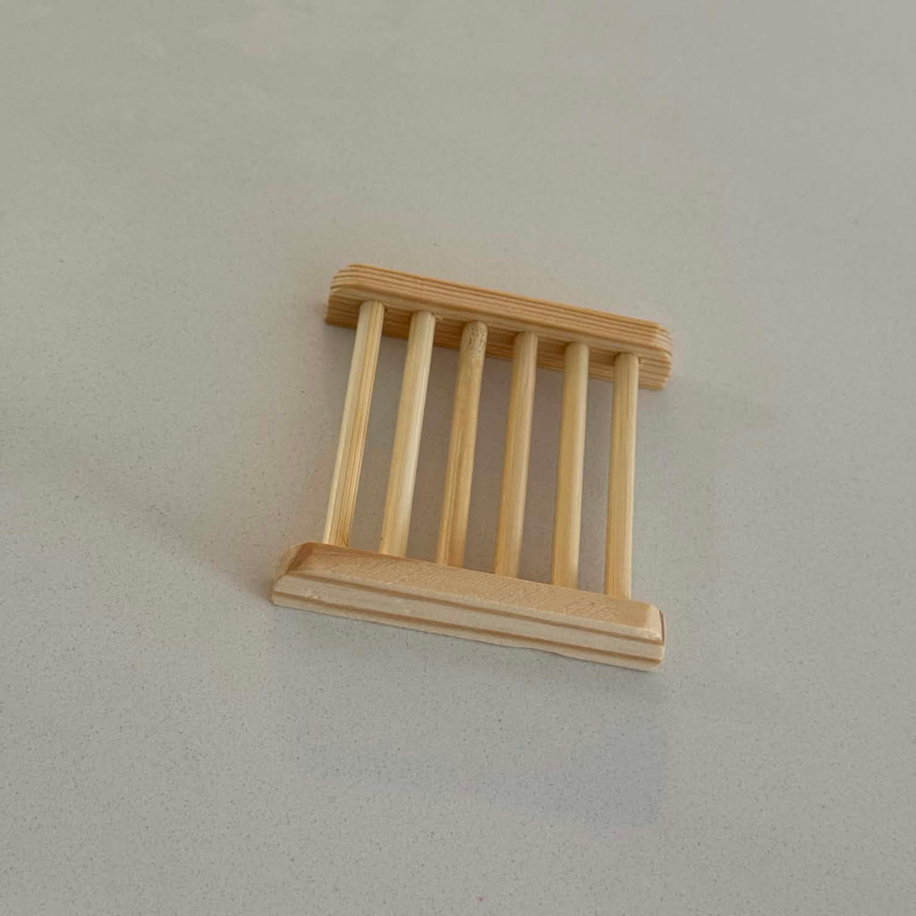 A miniature light natural wood slatted shelf or stand with a rectangular frame, photographed on a plain light gray surface.